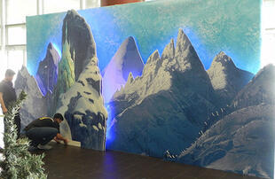 Workers assemble full size completed 3D mountain and castle display with lighting.